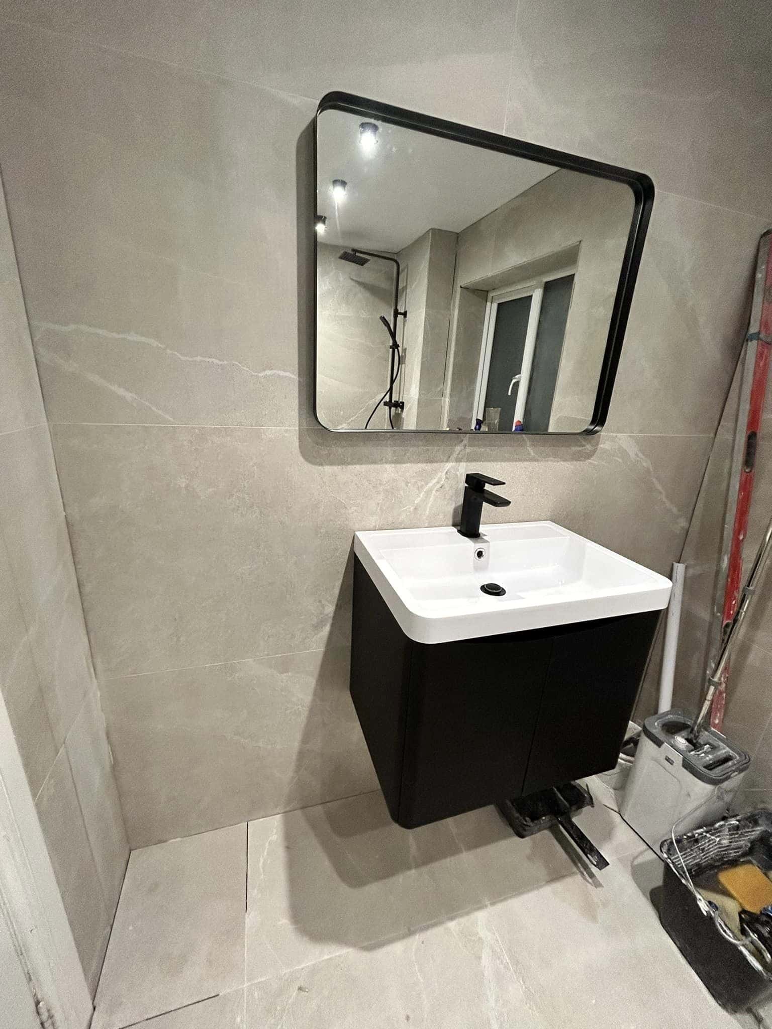 Modern bathroom sink with a black cabinet and a square mirror above it.