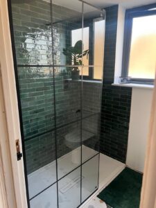 Modern shower with green tiles, glass door, and a plant on the windowsill.