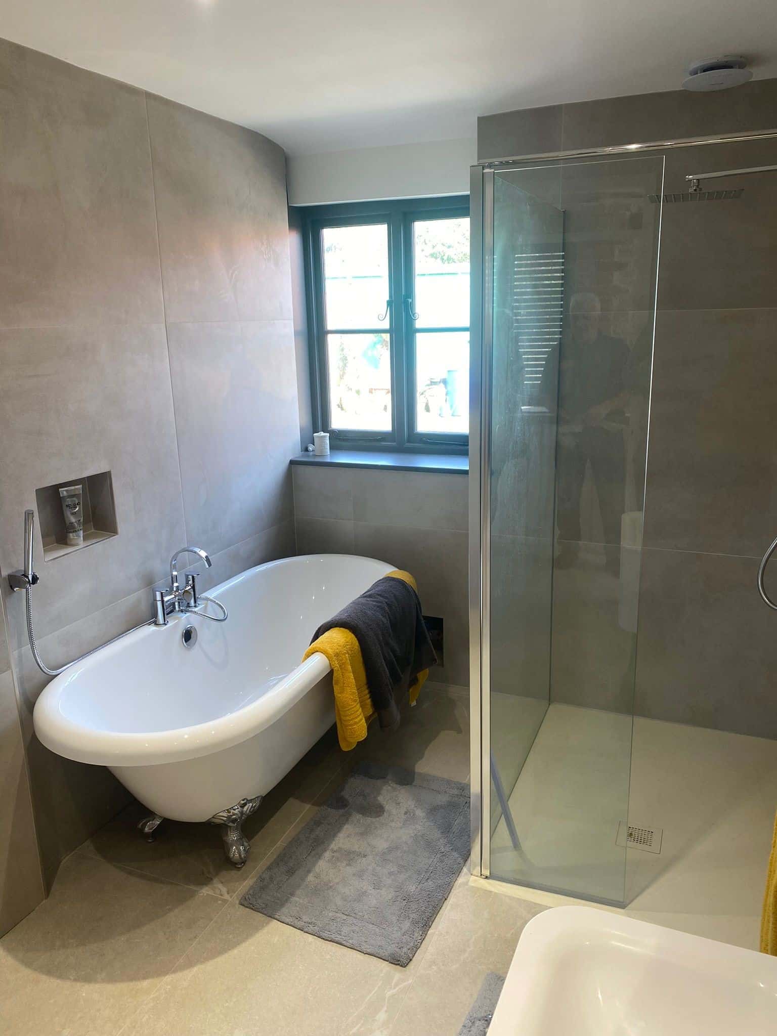 Modern bathroom with a bathtub, glass shower, window, and towels on the tub and floor.