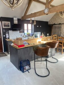 Modern kitchen with a wooden island, two brown chairs, and exposed beams.