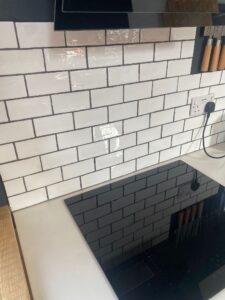White subway tile backsplash behind a kitchen stove with black countertop.