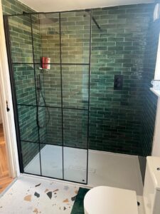 Modern shower with green tile walls, glass enclosure, and white bathroom fixtures.