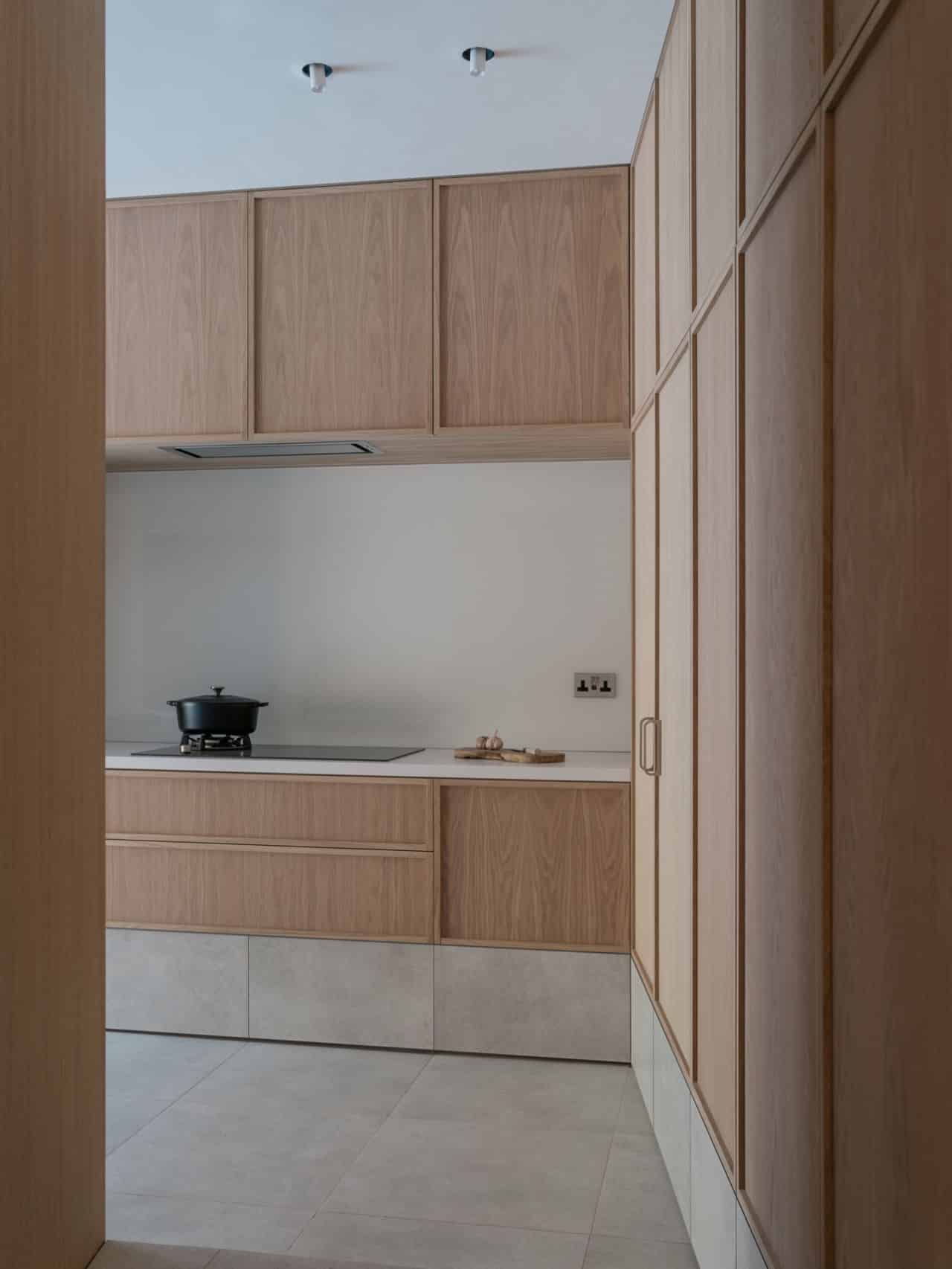 Minimalist kitchen with light wood cabinets and a countertop, viewed from a hallway.