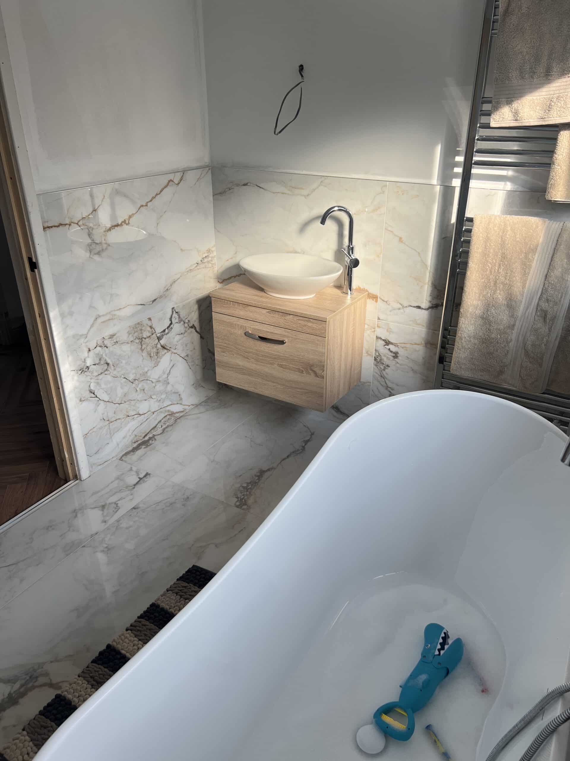 Modern bathroom with a white tub, marble walls, wooden sink cabinet, and towel rack.