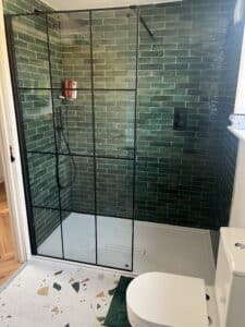 Modern bathroom with a glass shower, green tile wall, and a white toilet.