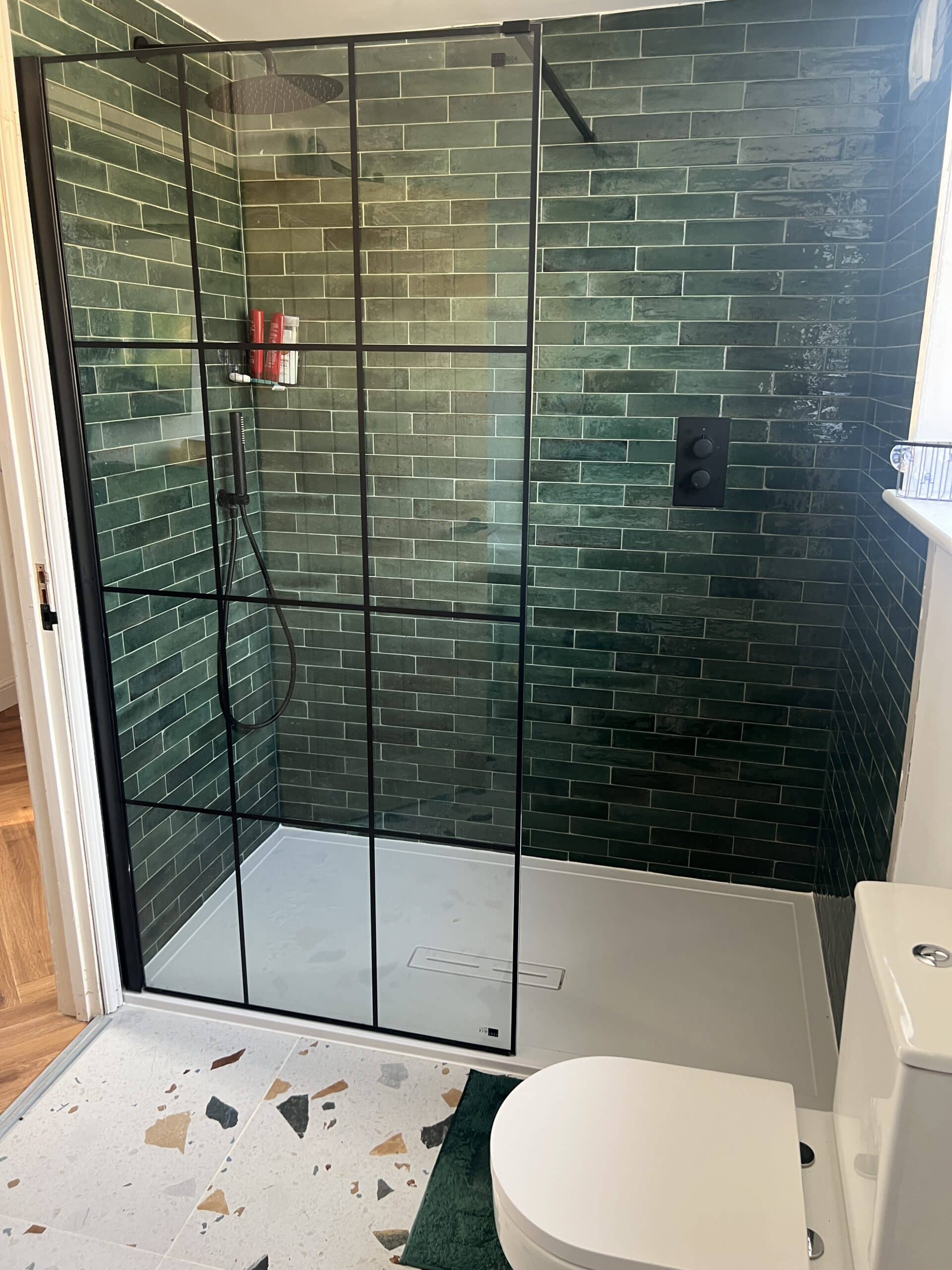 Modern bathroom with a glass shower, green tile wall, and a white toilet.