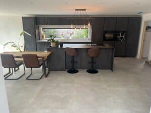 Modern kitchen with dark cabinets, island seating, a wooden table, and large window above the sink.