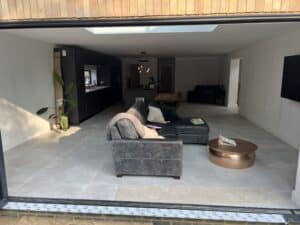 Modern open-plan living room with a gray sofa and copper coffee table, seen from outside.