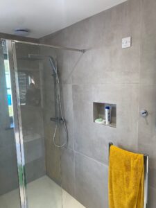 Modern shower with glass door, gray tile walls, and a yellow towel hanging on a rack.