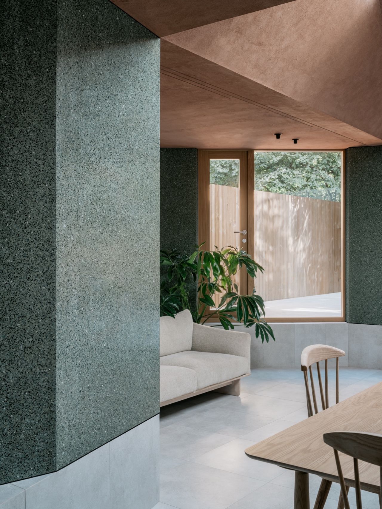 Modern living room with a sofa, plant, wooden table, chairs, and large window.