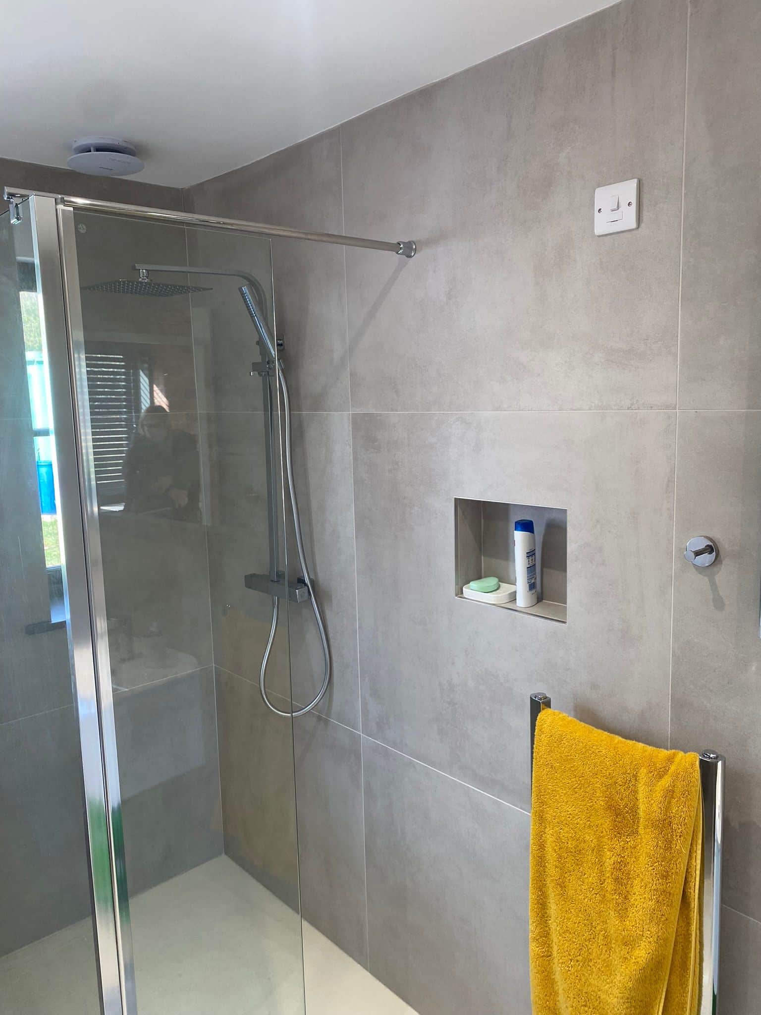 Modern shower with glass door, gray tile walls, and a yellow towel hanging on a rack.