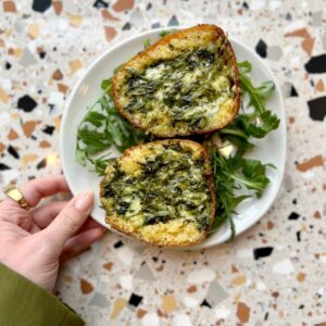 A hand holds a plate with two halves of stuffed bread filled with herbs, on a bed of arugula.