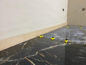 Black marble floor tiles with yellow spacers near a white wall and light-colored baseboard.