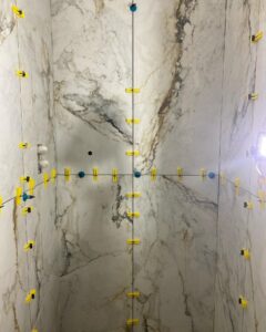 Marble tiles on a wall with yellow spacers and clips for tile installation.