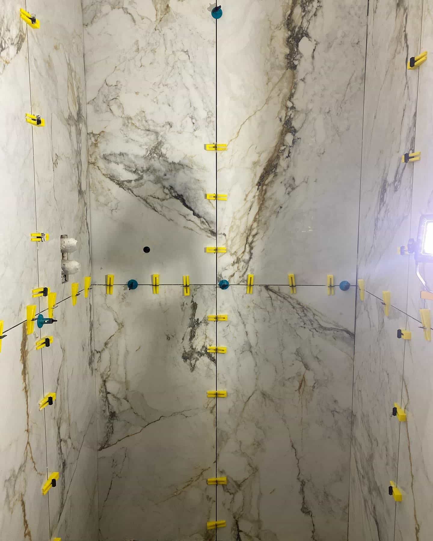 Marble tiles on a wall with yellow spacers and clips for tile installation.