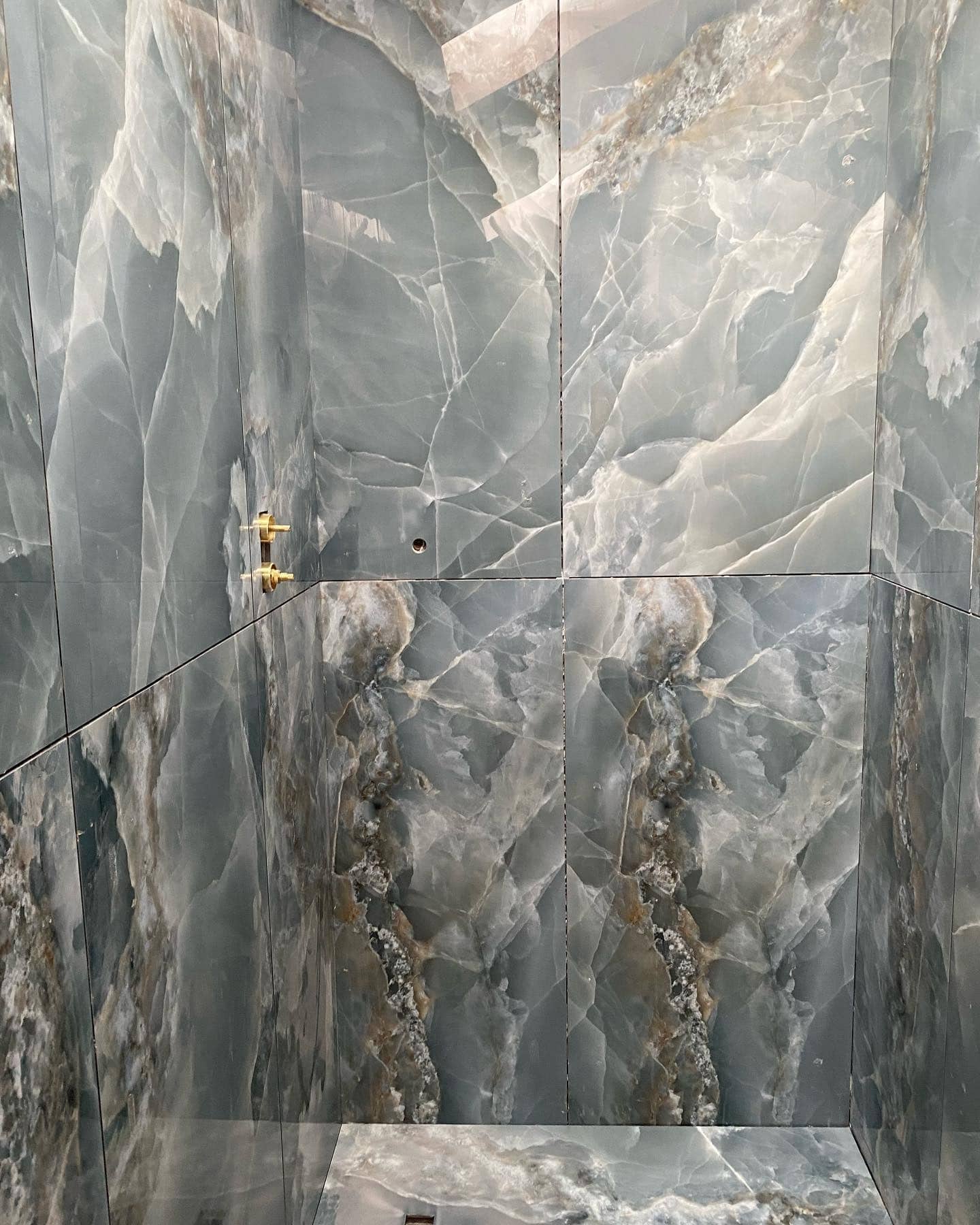 Gray and white marble shower with a sleek, modern design and brass shower fixture.