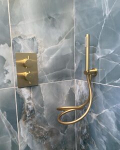 Gold shower controls and handheld shower head mounted on blue marble tiles.