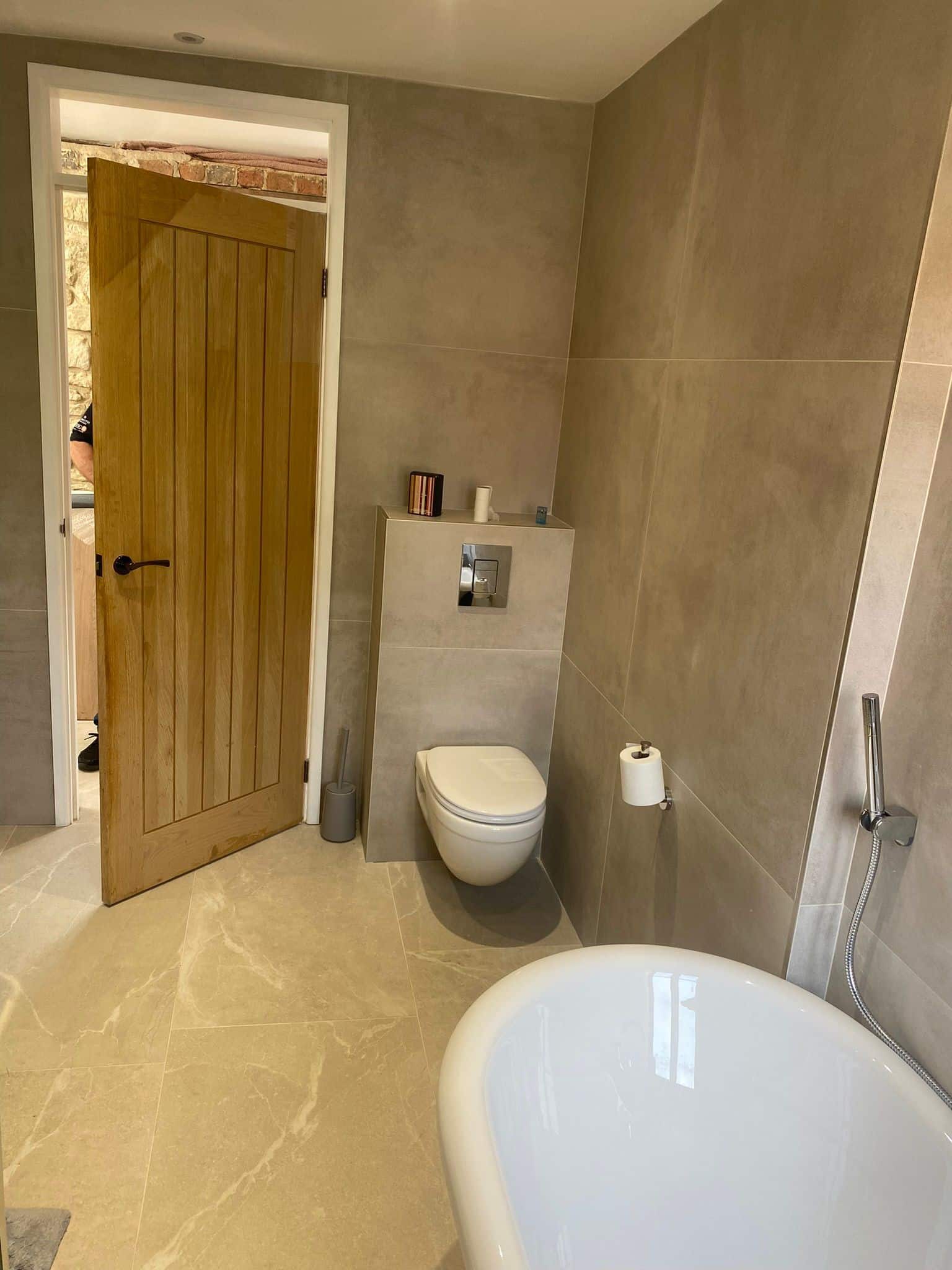 Modern bathroom with a bathtub, wall-mounted toilet, and a wooden door.