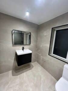 Modern bathroom with a wall-mounted sink, mirror, window, and partial view of a toilet.