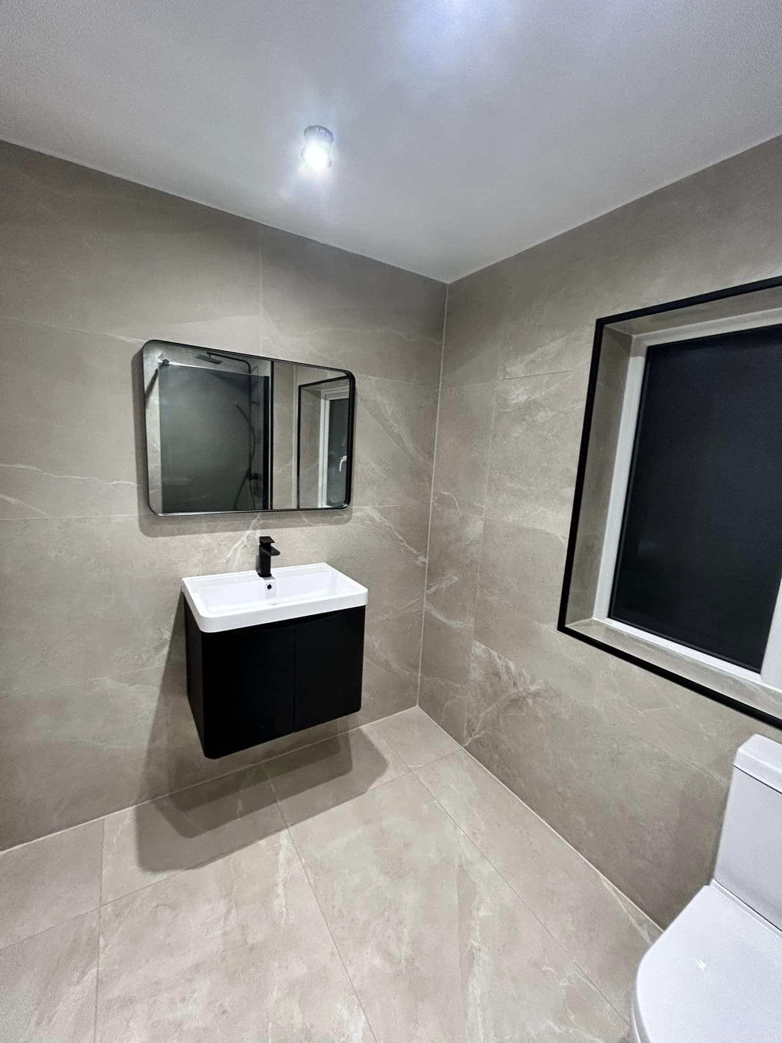 Modern bathroom with a wall-mounted sink, mirror, window, and partial view of a toilet.