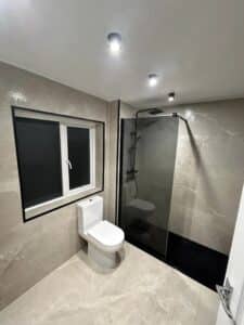 Modern bathroom with a toilet, large window, and walk-in shower with glass panel.
