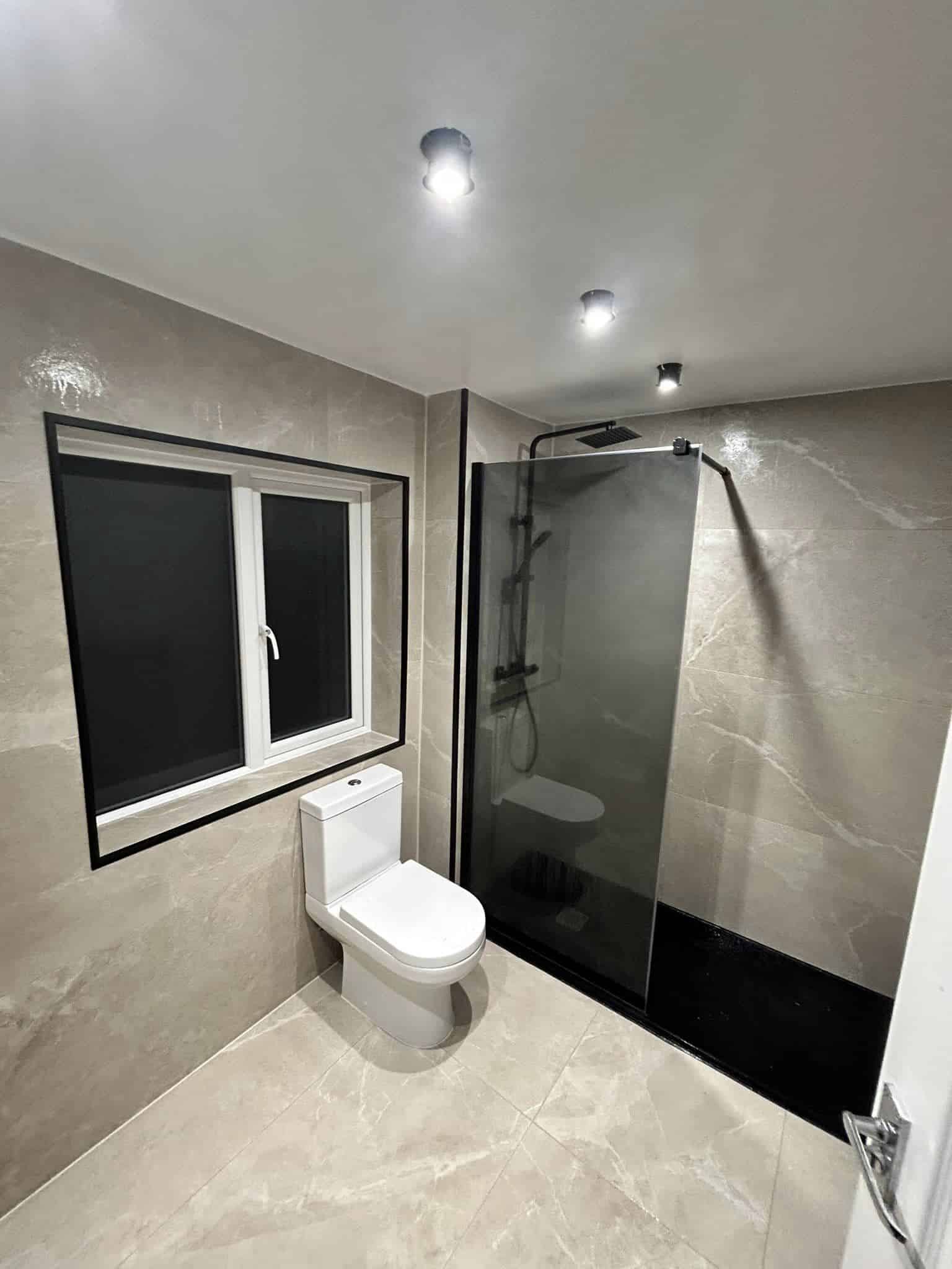Modern bathroom with a toilet, large window, and walk-in shower with glass panel.