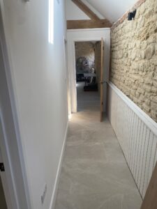 A hallway with white walls and a stone accent wall, leading to an open door at the end.