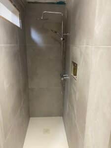 Small, modern shower with gray tiles, a rain showerhead, and a narrow frosted window.