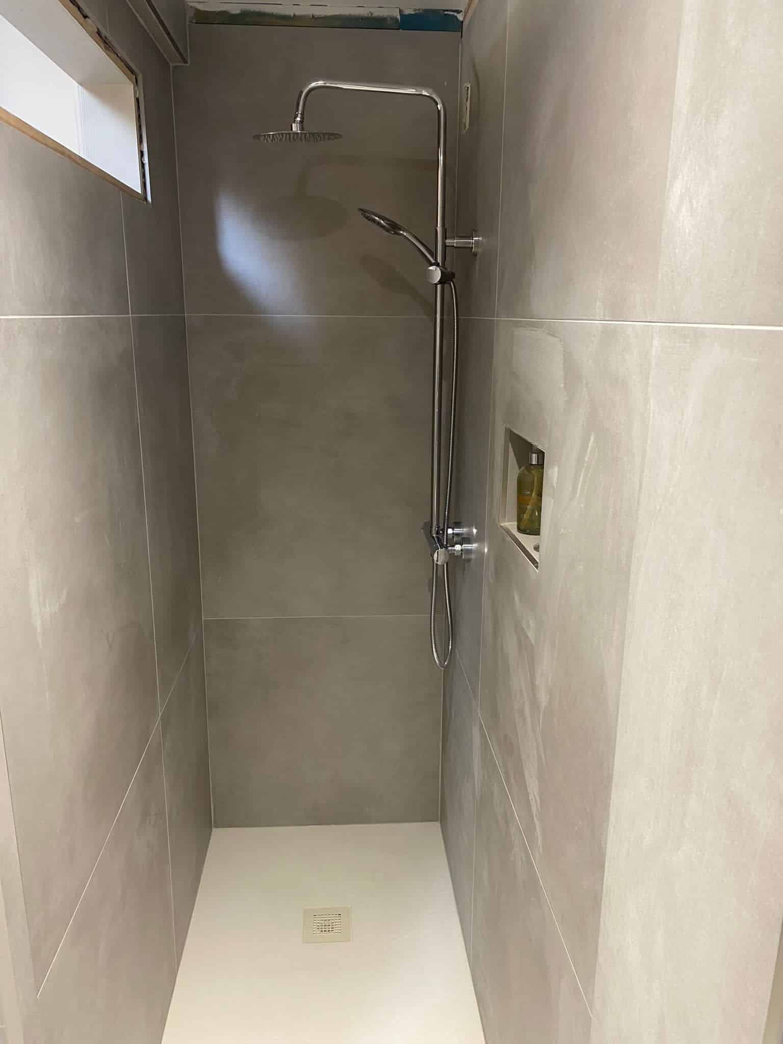Small, modern shower with gray tiles, a rain showerhead, and a narrow frosted window.
