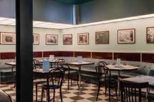 A cozy cafe with checkered floors, marble tables, and framed photos on pale green walls.