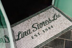Mosaic entrance sign reading "Lina Stores Ltd. Est. 1944" at a doorway.