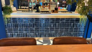 A modern bar counter with blue tiles and two brown chairs in the foreground.