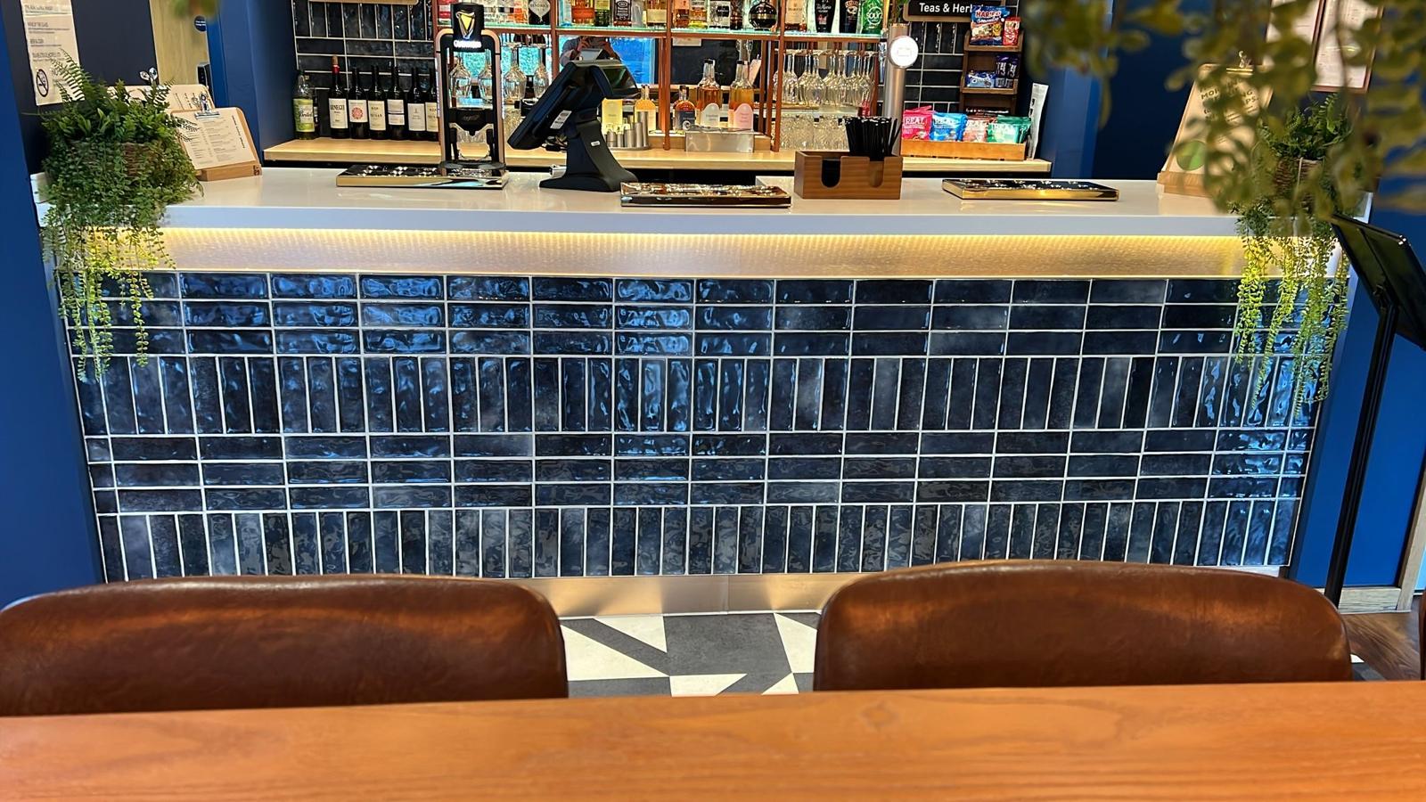 A modern bar counter with blue tiles and two brown chairs in the foreground.