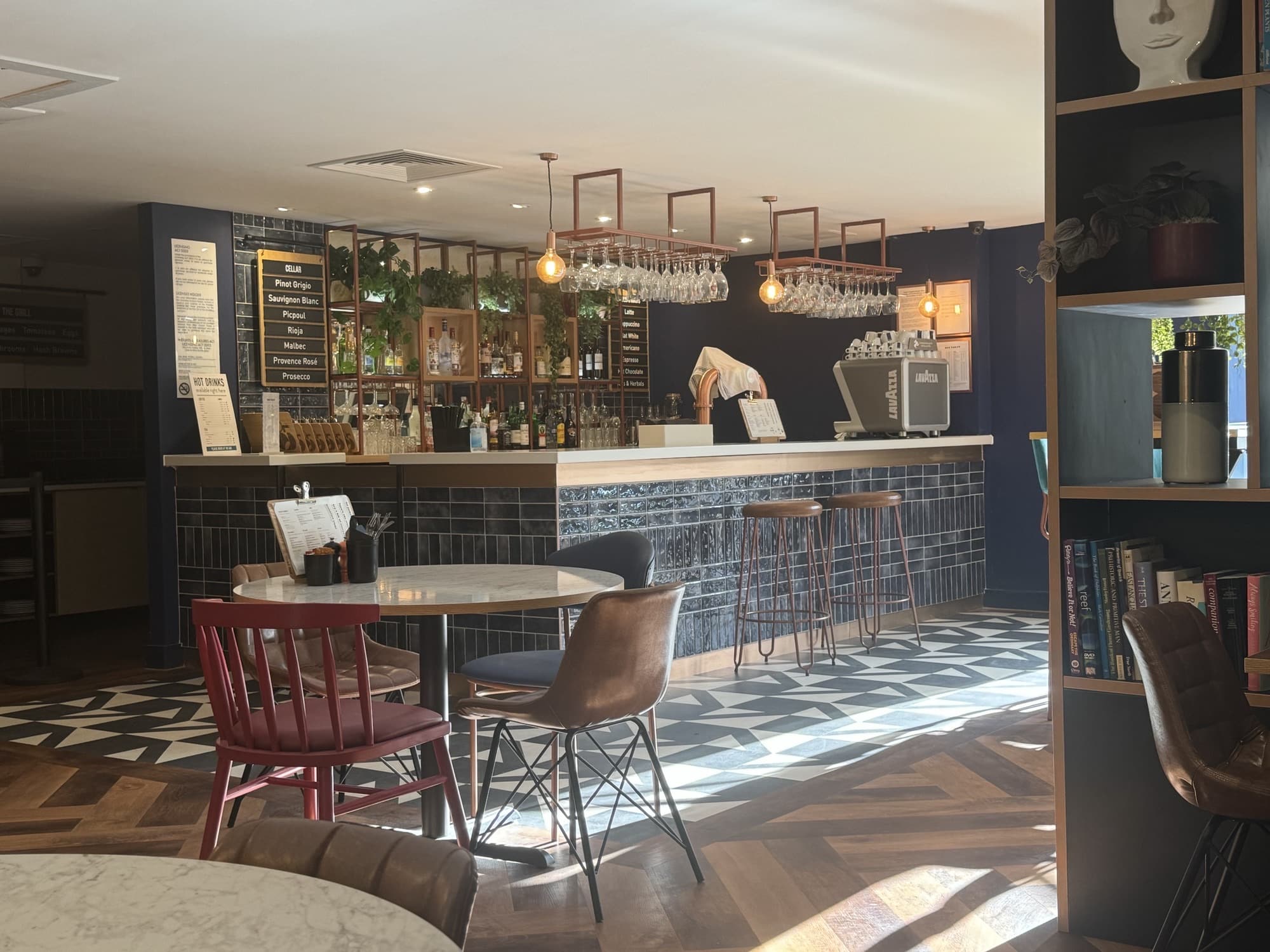 A modern bar interior with tables, chairs, and sunlight streaming through the windows.