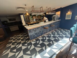 Modern bar with geometric patterned floor, bar stools, and blue walls with framed artwork.