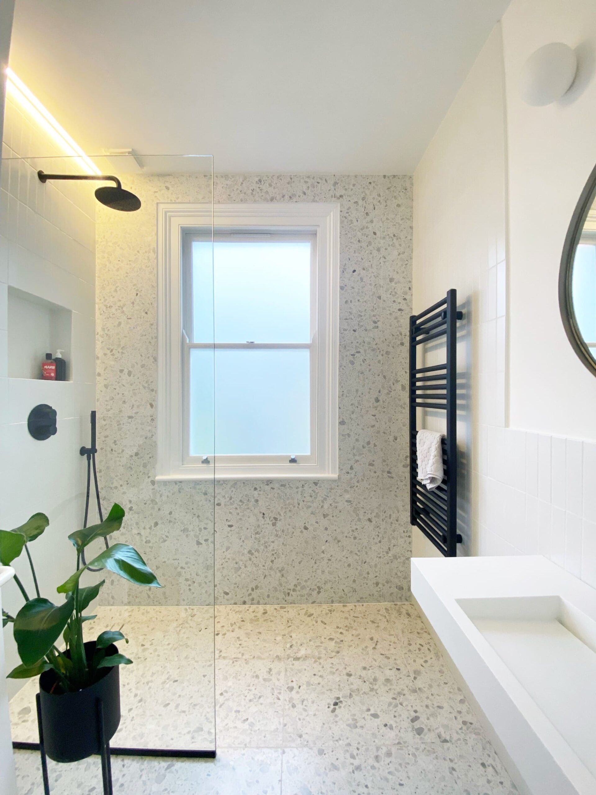 Modern bathroom with terrazzo tiles, a window, black towel rack, and a potted plant.