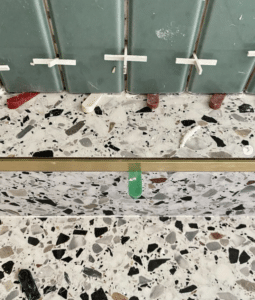 Green tiles being installed above a terrazzo countertop with spacers and leveling clips in place.