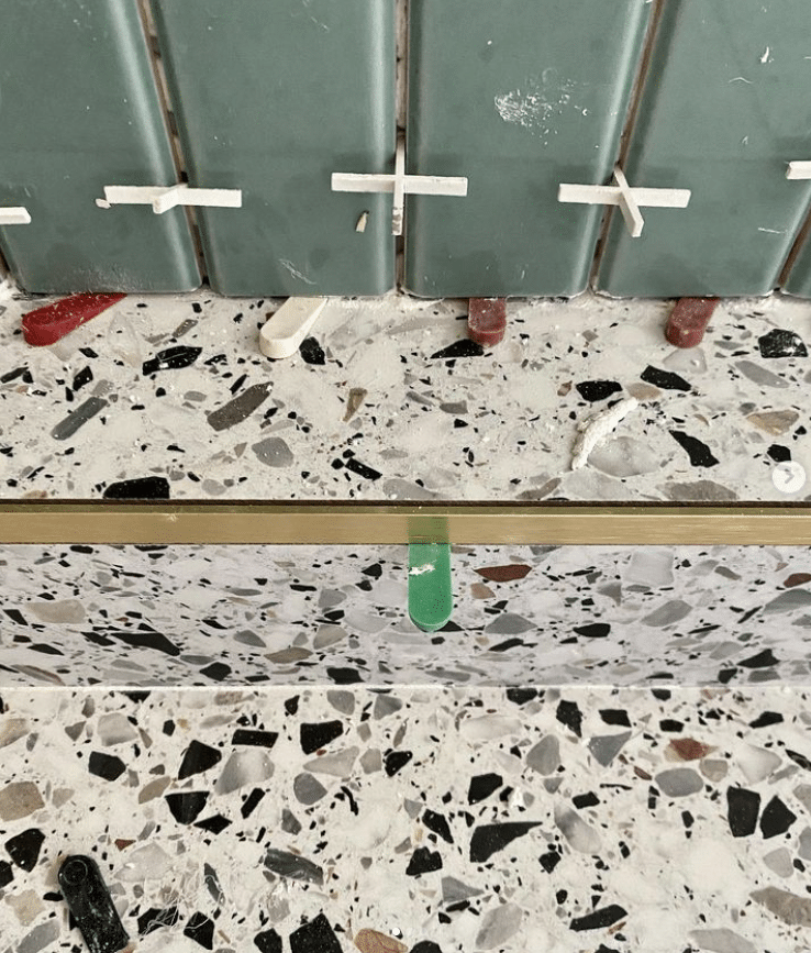 Green tiles being installed above a terrazzo countertop with spacers and leveling clips in place.