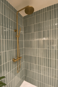 Gold shower fixture against light blue vertical tile walls.