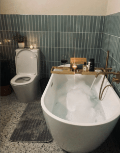 Modern bathroom with a freestanding tub, candles, wine, and green tile walls.