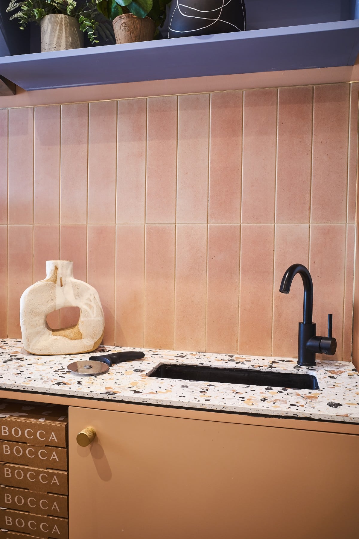 Modern kitchen counter with terrazzo surface, black faucet, pizza cutter, and decorative vase.
