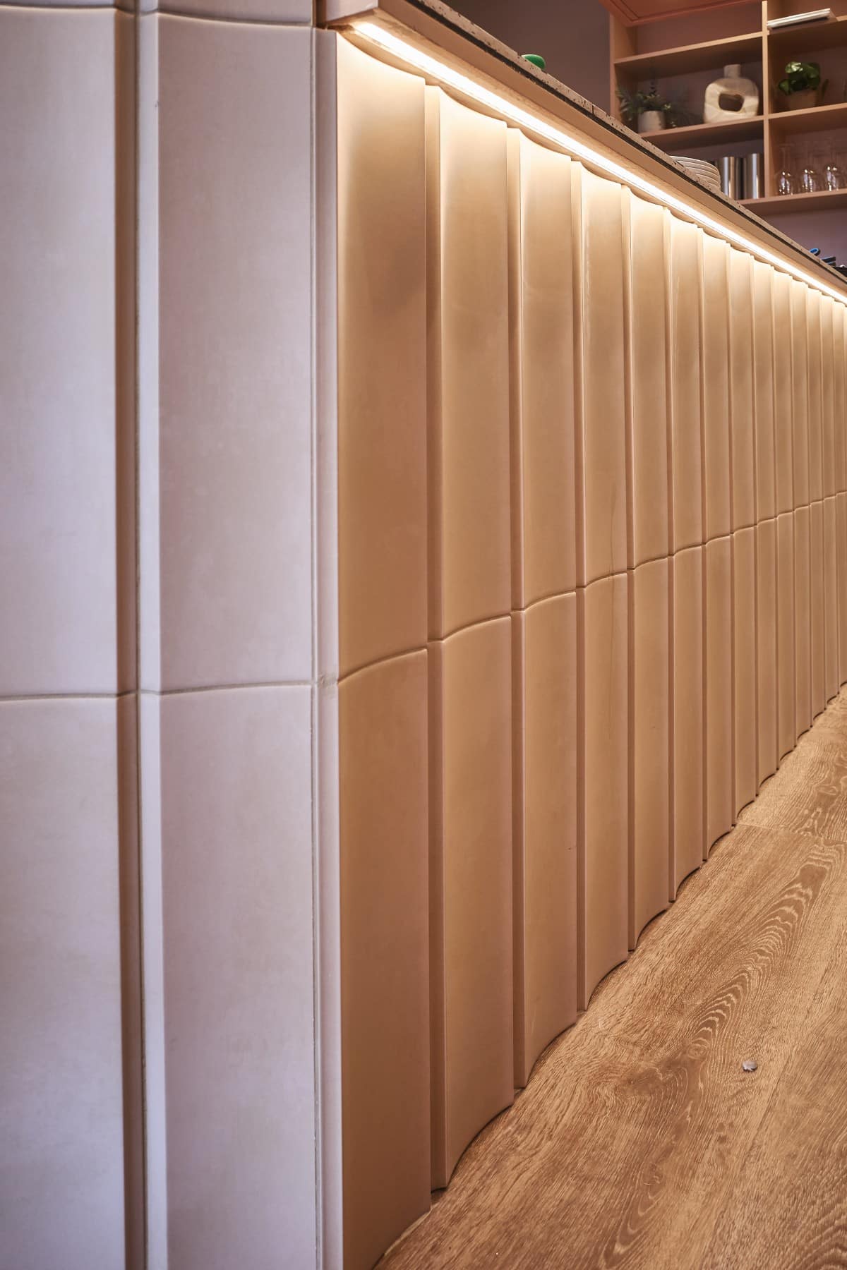 Textured beige wall panels with under-counter lighting next to a wooden floor.