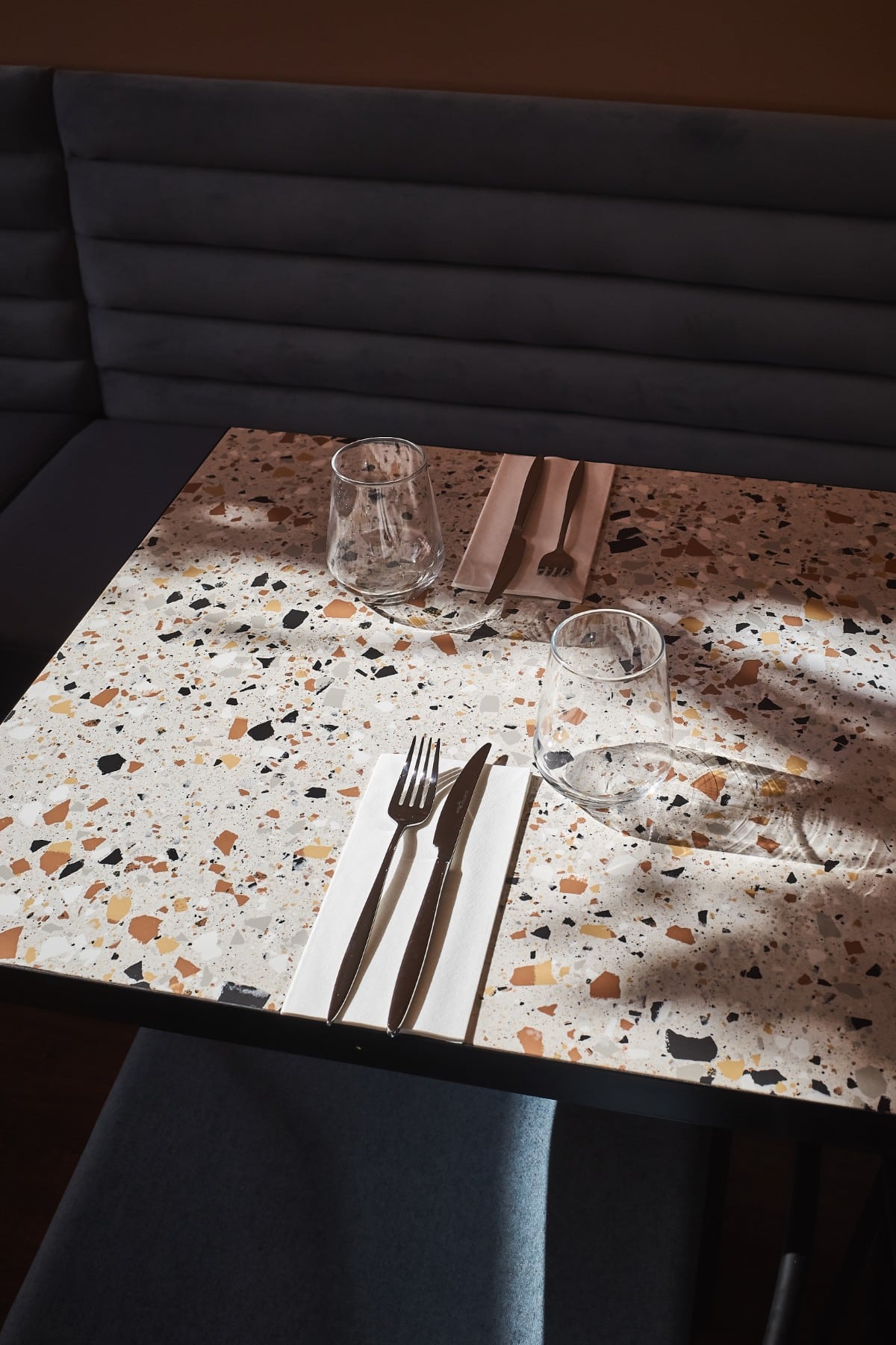 Terrazzo table set for two with glasses, cutlery, and napkins in a modern restaurant.