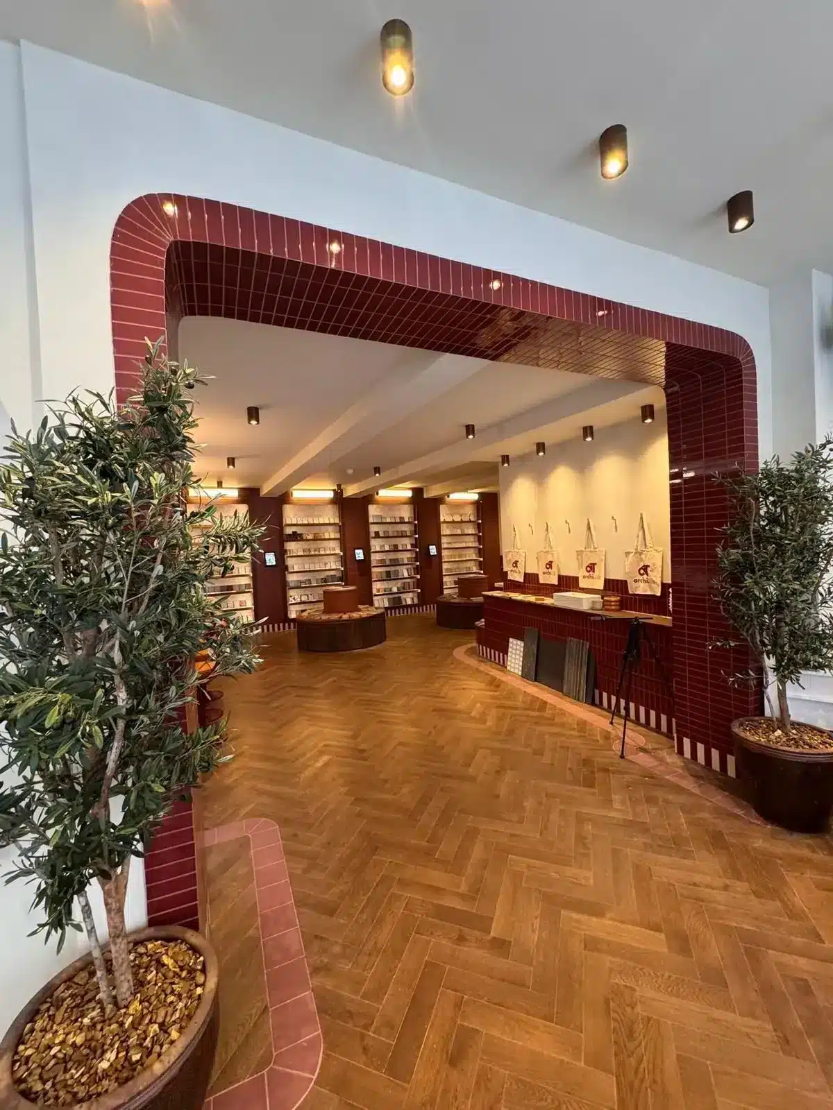 Modern showroom with wood herringbone floor, red tiled arch, and indoor plants at the entrance.