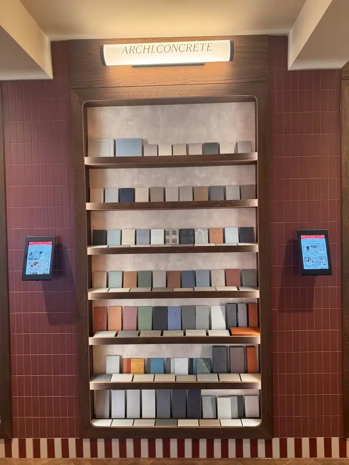 A display of concrete samples on shelves with two tablets on either side in a showroom.