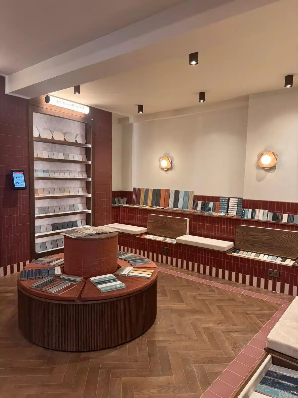 Showroom with sample tiles displayed on shelves, benches, and a circular table, with warm lighting.