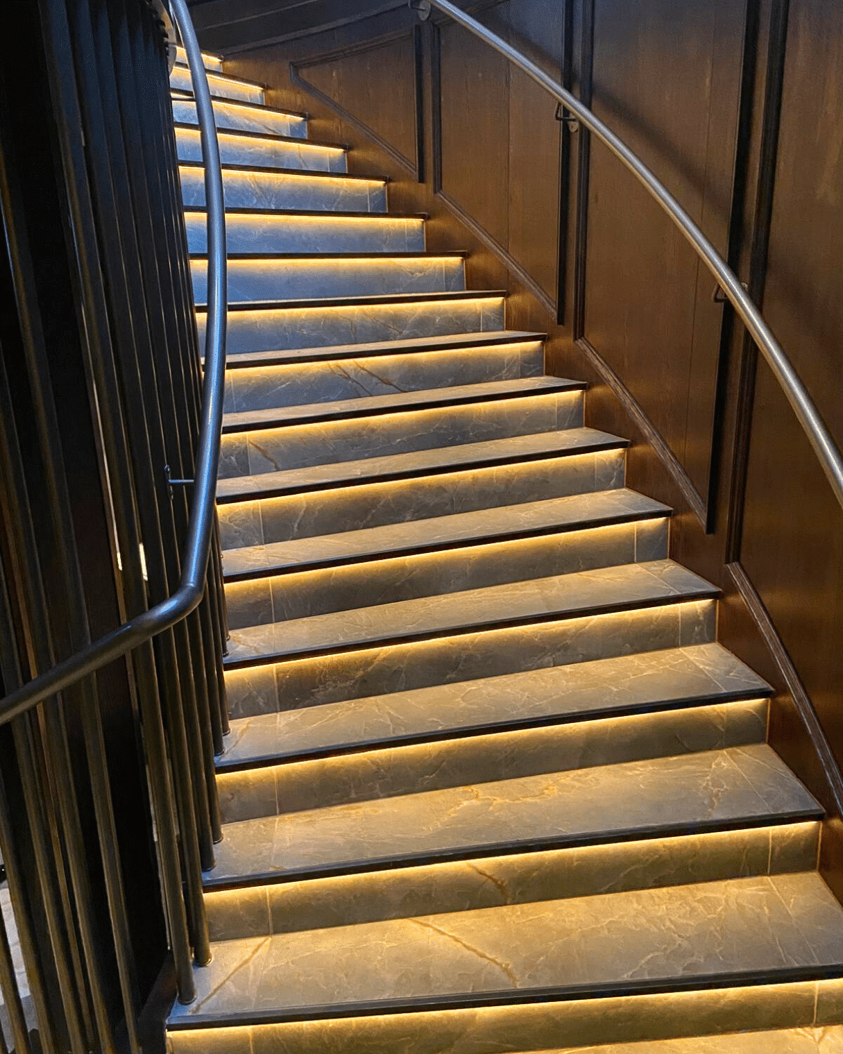 Curved staircase with gold lighting under each step and metal railings on both sides.