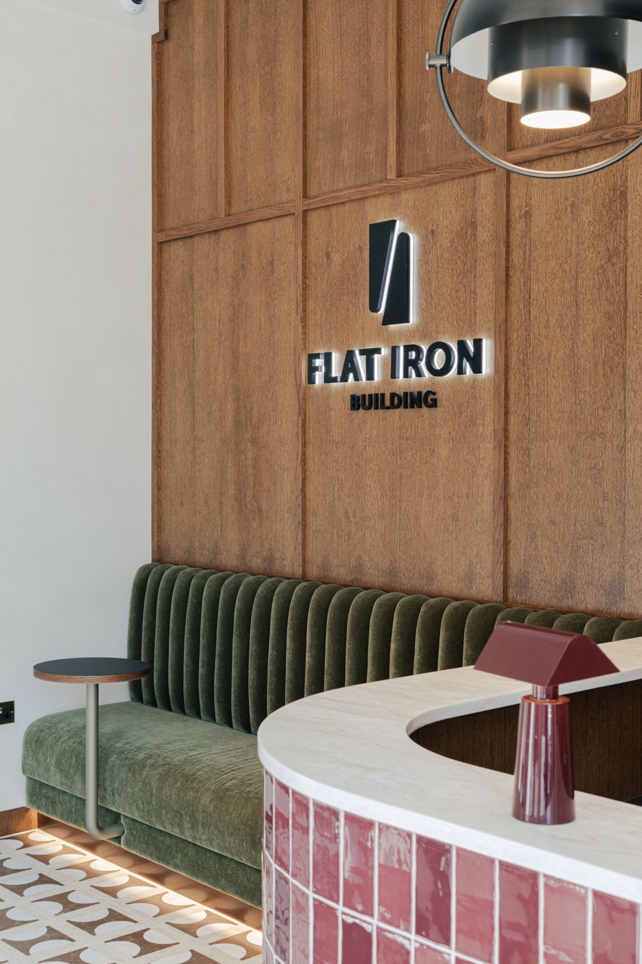 Lobby area with a curved desk, green seating, wood wall, and Flat Iron Building sign.