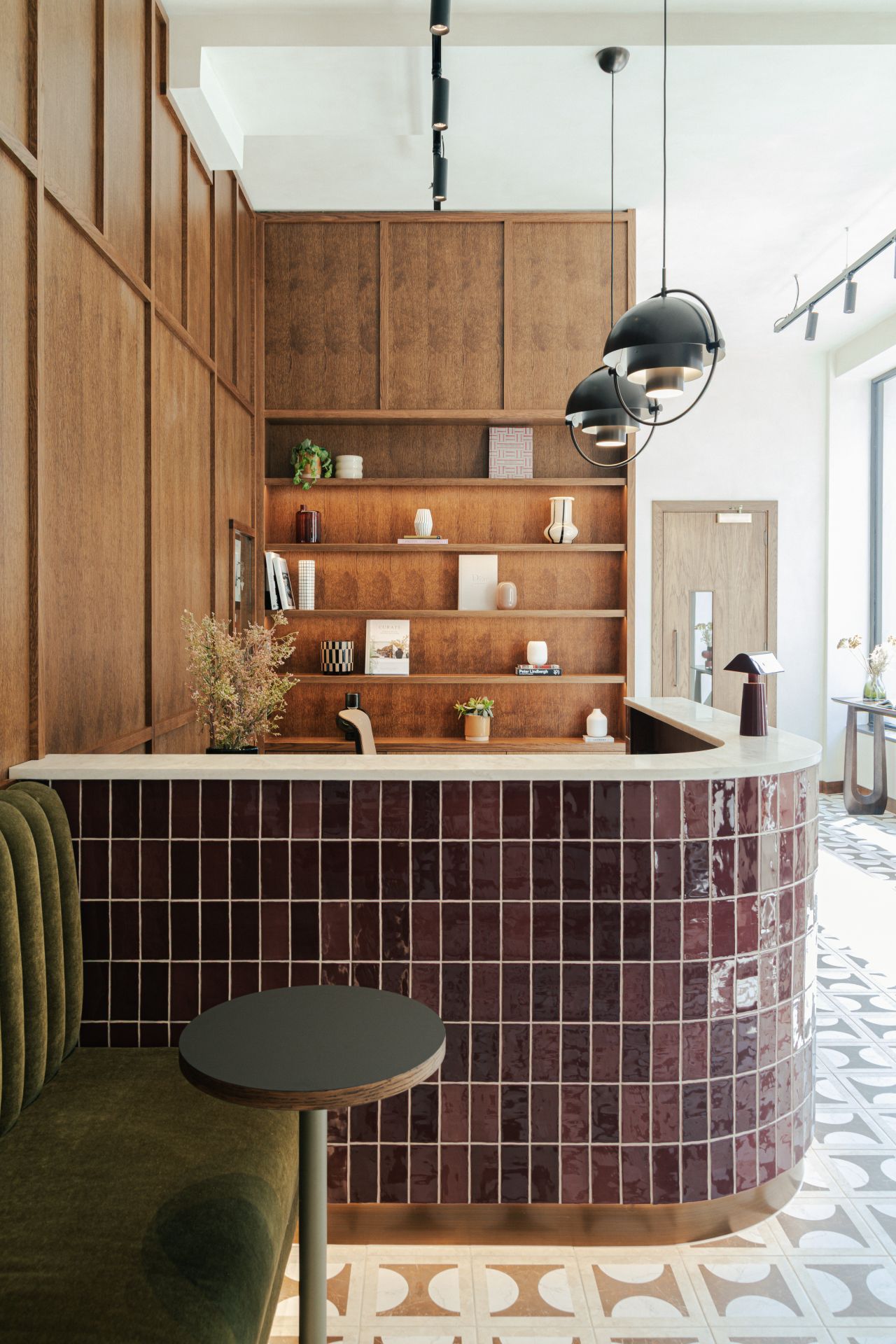 Modern reception area with a tiled front desk, wooden shelves, and patterned floor tiles.