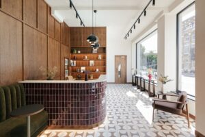Modern lobby with patterned floor tiles, wood paneling, a reception desk, and large sunny windows.